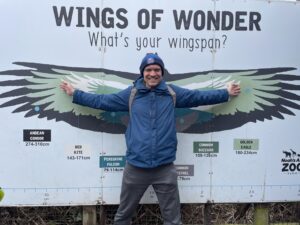 Alex Rawlings, standing in front of a sign with an image of wings on it